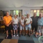 Groupe de golfeurs se réunissant dans un clubhouse après un tournoi de golf. Plusieurs participants, hommes et femmes, posent ensemble avec un trophée en argent, symbolisant leurs réalisations sportives. L'environnement est accueillant, avec un bar en arrière-plan et des décorations liées au golf sur les murs. L'événement met en avant l'esprit d'équipe et la camaraderie des joueurs passionnés de golf.
