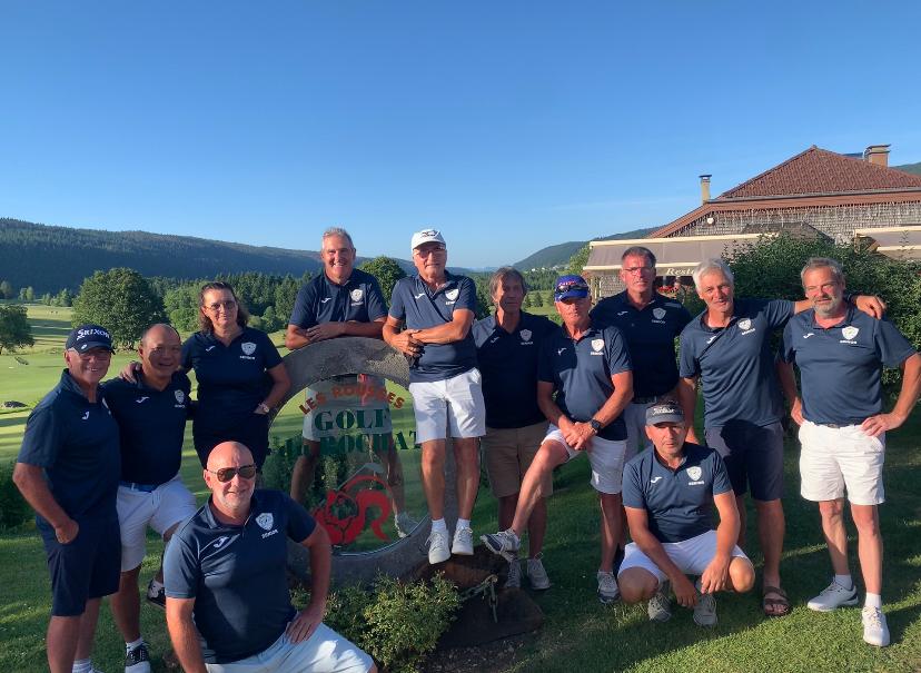Groupe de golfeurs posant devant le panneau du Golf du Haut-Doubs lors d'une belle journée ensoleillée. Les membres portent des polos identiques, affichant l'unité de l'équipe. En arrière-plan, le paysage verdoyant et les montagnes créent une atmosphère idéale pour le golf. Cette image illustre la camaraderie et la passion pour ce sport en plein air.