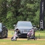 Deux voitures Audi haut de gamme stationnées sur un terrain de golf, avec un drapeau Audi flottant à proximité. Au premier plan, un chariot de golf avec des clubs, tandis qu'un paysage verdoyant entoure la scène. L'image évoque une atmosphère de luxe et de loisirs, idéale pour les passionnés de golf et d'automobiles.