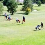 Groupe de golfeurs sur un parcours verdoyant, profitant d'une journée ensoleillée. Des adultes et des enfants marchent avec des chariots de golf, prêts à jouer. L'environnement est paisible, entouré d'arbres et de pelouses bien entretenues, reflétant une atmosphère conviviale et familiale propice à la pratique du golf.