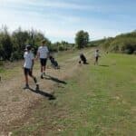 Jeunes golfeurs sur un parcours verdoyant, profitant d'une journée ensoleillée. Deux garçons marchent avec des sacs de golf, tandis qu'un autre se prépare à frapper une balle. L'environnement naturel, avec des arbres en arrière-plan, souligne l'importance des activités en plein air. Cette image illustre la passion pour le golf chez les jeunes et l'esprit de camaraderie sur le parcours.