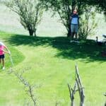Un jeune golfeur s'apprête à frapper une balle sur un parcours de golf verdoyant, sous un ciel ensoleillé. À proximité, un adulte observe avec un chariot de golf équipé, tandis que des arbres bordent le terrain. Cette scène illustre la passion du golf, idéale pour les familles et les jeunes joueurs souhaitant s'initier à ce sport.