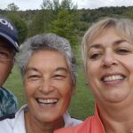 Quatre amis prennent un selfie sur un parcours de golf, souriant joyeusement. L'homme à gauche tient un driver de golf, tandis que les autres affichent des tenues sportives décontractées. En arrière-plan, on aperçoit un paysage verdoyant avec des arbres et des collines. Cette image illustre un moment convivial et détendu, parfait pour les passionnés de golf et les amateurs de loisirs en plein air.