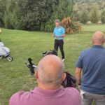 Groupe de golfeurs rassemblés sur un parcours, attentifs à un instructeur qui donne des conseils sur le jeu. Les participants, d'âges variés, portent des tenues de golf et ont des sacs de golf à leurs côtés. L'environnement est verdoyant, avec des arbres en arrière-plan, créant une atmosphère conviviale et propice à l'apprentissage. Cette scène illustre l'importance de la formation et du partage d'expériences dans le