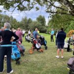 Groupe de golfeurs réunis sur un parcours, écoutant un discours donné par un instructeur. Plusieurs chariots de golf sont visibles, ainsi que des participants de différents âges, habillés de manière décontractée. L'événement semble être une séance d'initiation ou un briefing avant une compétition, dans un cadre verdoyant et agréable.