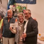 Cérémonie de remise de prix dans un club de sport, avec un groupe de personnes souriantes. Au centre, un homme et une femme se tiennent côte à côte, tenant un certificat. En arrière-plan, des objets de sport sont exposés sur les murs. L'événement se déroule dans une ambiance conviviale, avec des participants assis et des décorations sportives visibles. Cette image illustre la camaraderie et l'esprit d'équipe au sein du club.