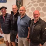 Groupe d'hommes et de femmes réunis lors d'un événement social, probablement lié au golf, dans un espace décoré avec des équipements de sport. Les participants, souriants, affichent une ambiance conviviale. En arrière-plan, on peut apercevoir des bouteilles de vin sur une table, suggérant que des rafraîchissements étaient offerts. L'image met en avant l'esprit communautaire et le plaisir partagé lors de cette rencontre.