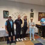 Photo d'un groupe de golfeurs réunis lors d'un événement convivial. On peut voir quatre participants, souriants, posant ensemble dans un cadre intérieur. À l'arrière-plan, des éléments décoratifs liés au golf, ainsi qu'une table avec des documents et des prix. L'ambiance est détendue et festive, typique des compétitions de golf amicales. Cette image illustre l'esprit communautaire et le plaisir de jouer au golf.