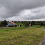 Paysage verdoyant d'un parcours de golf avec ciel nuageux, mettant en avant un chemin sinueux et des bâtiments en arrière-plan. L'image capture l'harmonie entre la nature et l'urbanisme, idéale pour les amateurs de golf et de plein air. Ce cadre paisible invite à la détente et aux activités sportives en extérieur.