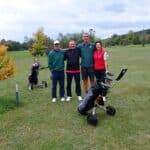 Quatre golfeurs posent sur un parcours verdoyant, entourés d'arbres aux feuilles jaunes, typiques de l'automne. Ils se tiennent près de leurs sacs de golf, prêts à jouer. L'atmosphère est conviviale et détendue, idéale pour une journée de golf. Ce moment capture l'esprit du sport et les plaisirs d'une sortie entre amis sur le green.