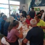 Groupe de golfeurs réunis autour d'une table pour partager un repas dans un club de golf. L'ambiance est conviviale, avec des échanges animés entre les participants. En arrière-plan, des éléments liés à la Ryder Cup 2018 sont visibles, soulignant l'importance de cet événement dans le monde du golf. Les convives dégustent des mets variés, accompagnés de boissons, tout en profitant de la camaraderie et de la passion pour le golf.