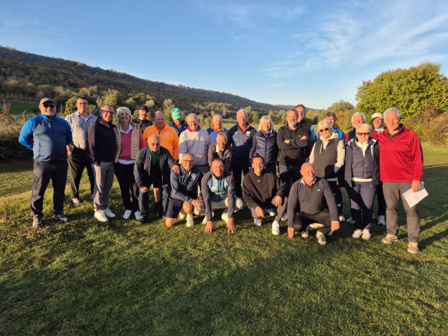 Groupe de golfeurs réunis sur un parcours, posant ensemble sous un ciel dégagé. L'arrière-plan présente des collines verdoyantes et des arbres aux couleurs d'automne. Les participants, d'âges variés, portent des vêtements de golf adaptés à la saison, et affichent des sourires, témoignant d'une ambiance conviviale. Cette image illustre un événement de golf communautaire, mettant en avant la camaraderie et le plaisir du sport en plein
