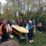 Groupe de personnes rassemblées lors d'un événement convivial en plein air, avec une grande table dressée au milieu de la nature. Des participants discutent et se divertissent, tandis que des bouteilles de vin et des verres sont visibles sur la table. L'ambiance est détendue, avec des vêtements adaptés à la saison automnale. Cette image illustre un moment de camaraderie et de célébration, idéal pour promouvoir des activités de groupe en extérieur, des événements communautaires ou