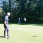 Un groupe de golfeurs sur un green, avec un joueur en train de préparer un putt. L'environnement est verdoyant, entouré d'arbres, et la scène se déroule sous un ciel ensoleillé. Les golfeurs portent des vêtements de sport adaptés, créant une atmosphère conviviale et détendue propice à la pratique du golf. Ce moment capture l'essence du jeu, alliant compétition et camaraderie sur le parcours.