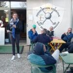 Une événement convivial se déroule à l'Association Sportive Golf des Saisons, où une intervenante présente des informations aux membres. Plusieurs personnes sont assises autour de tables colorées, écoutant attentivement. L'atmosphère est détendue et conviviale, avec des participants de différents âges, tous engagés dans la vie du club. Le logo de l'association est bien visible en arrière-plan, soulignant l'importance de la communauté golfique locale.