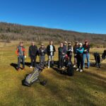 Groupe de golfeurs sur un terrain de golf par une journée ensoleillée. Les participants, vêtus de vêtements de golf appropriés, posent ensemble avec leurs sacs de golf et chariots. En arrière-plan, une nature verdoyante et des collines. Cette image illustre une sortie de golf conviviale, idéale pour les passionnés de ce sport.