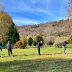 Groupe de personnes jouant au golf sur un parcours verdoyant en automne, entouré d'arbres aux feuilles dorées. Le ciel est clair avec quelques nuages, créant une atmosphère agréable pour les activités de plein air. Les participants semblent concentrés sur leur jeu, profitant d'une journée ensoleillée dans un cadre naturel. Cette scène évoque la convivialité et le plaisir de pratiquer le golf en groupe.