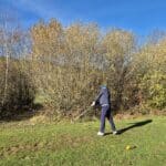 Un golfeur se prépare à frapper une balle sur un parcours de golf en automne. L'arrière-plan est composé d'arbres aux feuilles jaunies, typiques de la saison, sous un ciel bleu clair. Le joueur, vêtu d'une tenue de golf, se concentre sur son coup. Des tees de golf sont visibles au sol, indiquant le point de départ du trou. Cette image capture l'essence d'une journée de golf en plein air, mettant en