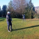 Deux golfeurs sur un parcours verdoyant, l'un se préparant à frapper la balle avec un club, tandis que l'autre observe. L'environnement est calme, avec des arbres en arrière-plan et un ciel clair, idéal pour une partie de golf. Cette image illustre parfaitement l'esprit du golf, alliant détente et concentration sur le terrain.