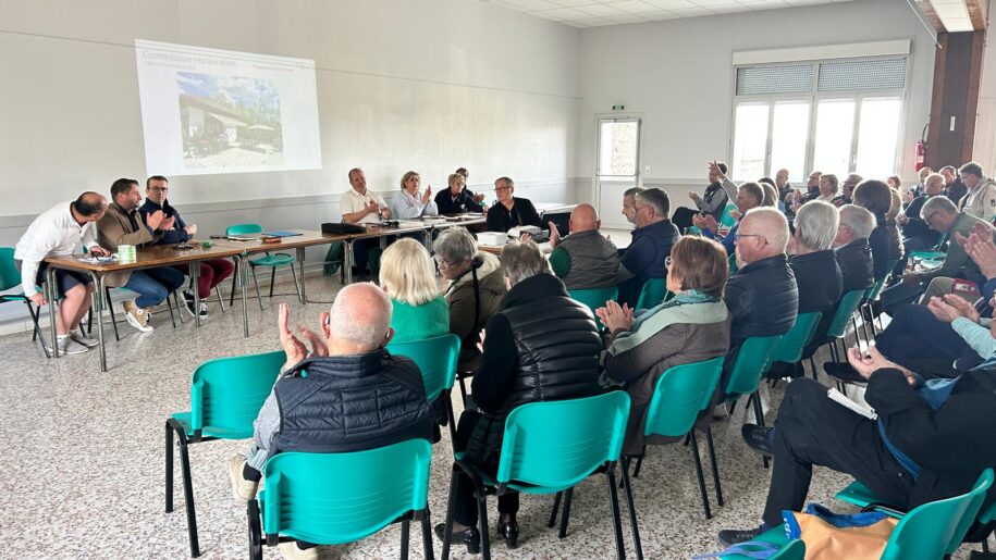 Réunion publique sur la restauration, avec une assistance active de la communauté. Un groupe de participants écoute attentivement les intervenants, qui discutent de projets de développement. Des applaudissements témoignent de l'intérêt et de l'engagement des membres présents. L'événement se déroule dans une salle lumineuse, favorisant les échanges et le partage d'idées.