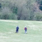 Groupe de golfeurs marchant sur un parcours verdoyant, poussant des chariots de golf. Arrière-plan boisé avec des arbres feuillus, indiquant un environnement naturel. Activité de plein air propice au sport et à la détente, idéale pour les amateurs de golf. Le terrain est bien entretenu, contribuant à une expérience de jeu agréable.