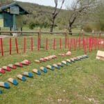 Image d'un terrain de golf d'extérieur avec des obstacles colorés. On peut voir des poteaux rouges dressés et des éléments en bois peints en bleu et rose disposés sur l'herbe. En arrière-plan, une cabane de golf offre un abri aux visiteurs. L'environnement est verdoyant, avec des arbres en pleine feuillaison, idéal pour une journée de loisirs en plein air. Parfait pour les amateurs de golf et les familles cherchant des activités ludiques