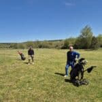 Deux golfeurs se tiennent sur un terrain de golf verdoyant par une belle journée ensoleillée. L'un des golfeurs, en tenue décontractée avec un chapeau, se prépare à jouer, tandis que l'autre, vêtu d'un ensemble sportif bleu, pose avec un chariot de golf. L'arrière-plan montre une nature luxuriante, avec des arbres et un ciel dégagé, créant une atmosphère agréable pour une partie de golf. Cette image ill