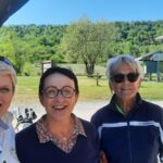 Trois femmes souriantes se tiennent devant un paysage verdoyant, probablement dans un cadre de loisirs en plein air. Elles sont vêtues de tenues décontractées adaptées à une activité de plein air. En arrière-plan, on aperçoit des panneaux directionnels et des installations, suggérant un lieu dédié à des activités comme le golf. Cette image évoque une ambiance conviviale et joyeuse, idéale pour le partage entre amis ou en famille dans un environnement naturel.