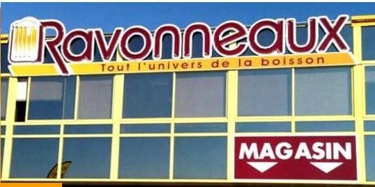 Image du magasin Ravonneaux, spécialisé dans la vente de boissons. La devanture est bien visible, avec un logo coloré et des fenêtres transparents qui laissent entrevoir l'intérieur. Le slogan Tout l'univers de la boisson souligne la variété des produits proposés. Le mot MAGASIN est affiché en rouge, attirant l'attention des clients potentiels. Cette image illustre un point de vente accueillant et dynamique pour les amateurs de boissons.